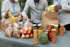 Bénévoles distribuant des denrées alimentaires variées (légumes, conserves, huile, fruits secs) lors d'une action de soutien alimentaire.