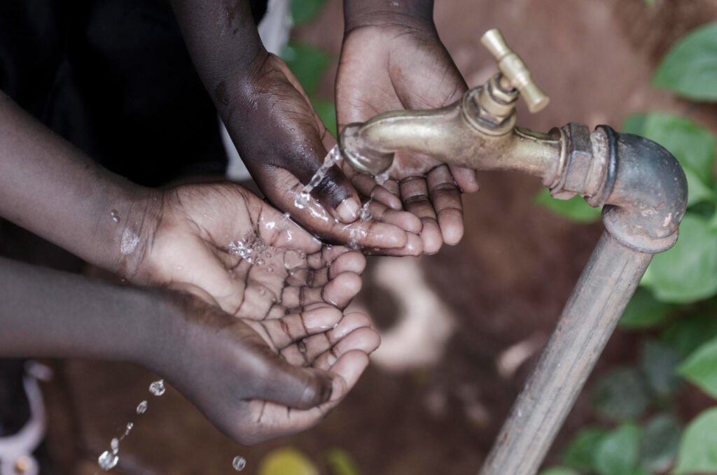 Mains d'enfants tendant pour recevoir de l'eau claire s'écoulant d'un robinet rouillé, symbolisant l'accès à l'eau potable.